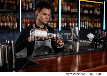 Bartender in apron adds ingredient to shaker 82035016