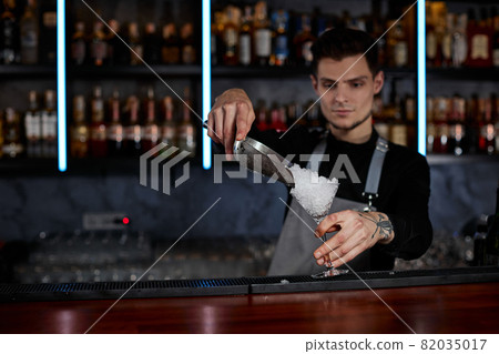 Barman puts the ice cubes into a glass 82035017