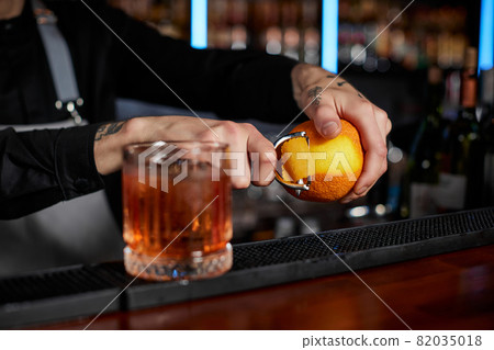 bartender makes a cocktail in a glass with orange peel 82035018