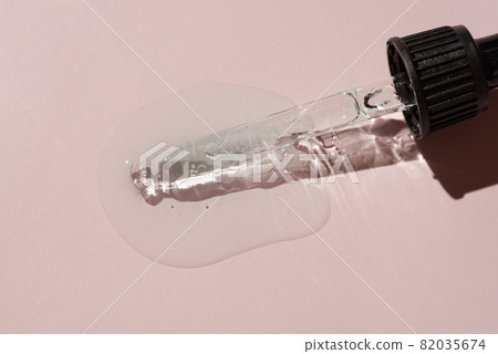 Liquid oil serum drop in pipette isolated on pastel pink background. Retinol, aha, bha acid, collagen skincare fluid, photo with shallow depth of field. Gold essence in dropper for beauty treatment 82035674