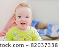 Full length of a baby girl smiling while sitting on the bed at home. Child, happiness and people concept - adorable baby 82037338