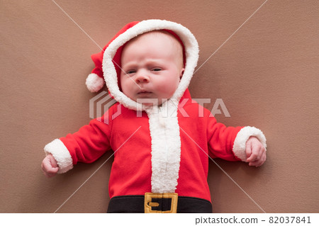 Newborn girl dressed in santa claus costume looking at camera with confused face. Newborn girl dressed in santa claus costume looking at camera with confused face. 82037841