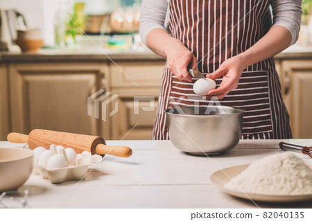 Young woman breaking egg over bowl with dough, close-up Young woman breaking egg over bowl with dough, close-up 82040135