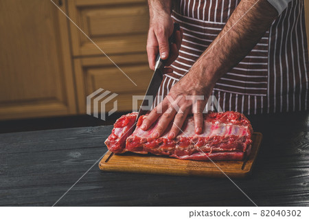 Man cuts of fresh piece of meat on a wooden cutting board in the home kitchen 82040302