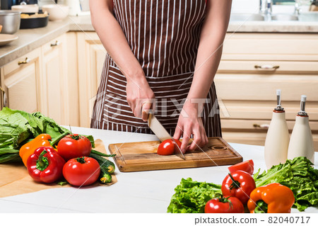 Young woman cooking in the kitchen at home. A woman cuts a tomato and vegetables with a knife. 82040717
