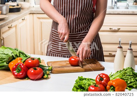 Young woman cooking in the kitchen at home. A woman cuts a tomato and vegetables with a knife. 82040725