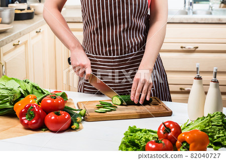 Young woman cooking in the kitchen at home. A woman cuts a cucumber and vegetables with a knife. 82040727
