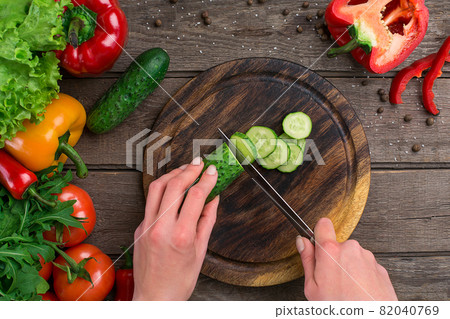 Female hands cutting cucumber at table, top view Female hands cutting cucumber at table, top view 82040769