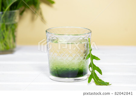 Green Chlorophyll or Chlorella drink in glass with water on white table, Orange Background. Green Drops in clear water, Antioxidant food and drinks. 82042841