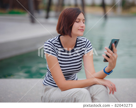 Portrait of young woman in park with smartphone Portrait of young woman in park with smartphone 82043273