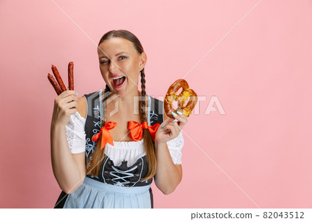 Adorable Oktoberfest woman, waitress wearing a traditional Bavarian or german dirndl holding bretzel isolated on pink studio background. 82043512