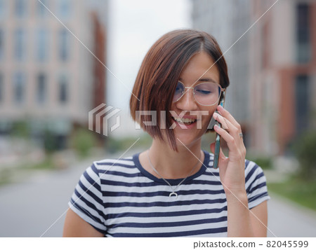 Smiling woman using mobile phone in the street Smiling woman using mobile phone in the street 82045599