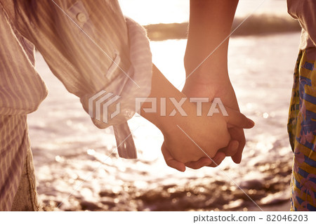 young couple lovers holding hands watching tide at beach young couple lovers holding hands watching tide at beach 82046203