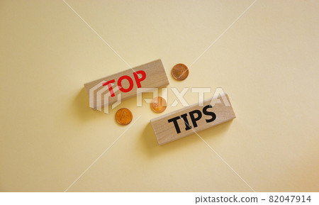 Top tips symbol. Concept words 'top tips' on wooden blocks on a beautiful white background, metallic coins. Business and top tips concept, copy space. 82047914