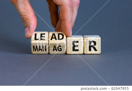 Manager versus leader symbol. Businessman flips wooden cubes and changes the word 'manager' to 'leader'. Beautiful grey background, copy space. Business and manager versus leader concept. Manager versus leader symbol. Businessman flips wooden cubes and changes the word 'manager' to 'leader'. Beautiful grey background, copy space. Business and manager versus leader concept. 82047955