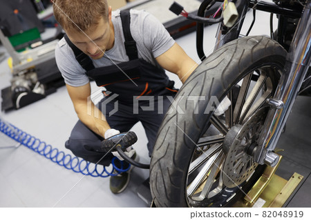 Man repairman inflating motorcycle tires in auto repair shop Man repairman inflating motorcycle tires in auto repair shop 82048919