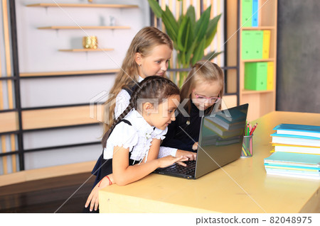Young female students in school uniforms before the lesson in the classroom. Children at the laptop in the classroom. Remote education. The company of schoolgirls in the classroom. Primary school Young female students in school uniforms before the lesson in the classroom. Children at the laptop in the classroom. Remote education. The company of schoolgirls in the classroom. Primary school 82048975