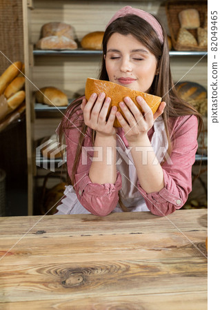 The shop assistant smells the bread and is delighted with the fantastic aroma. Attractive girl from the bakery shop. 82049465
