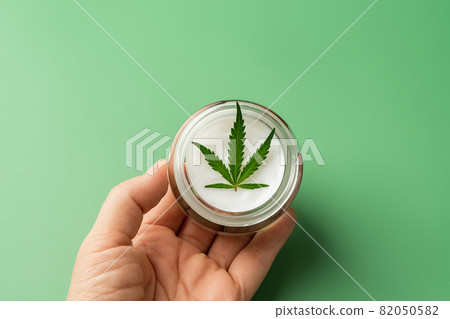 Moisturizer skin care cream with fresh cannabis sativa leaf in a woman hand palm on green background 82050582