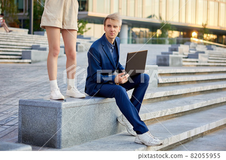 Female legs in shorts and man in business suit with laptop near office building. Female legs in shorts and man in business suit with laptop near office building. 82055955