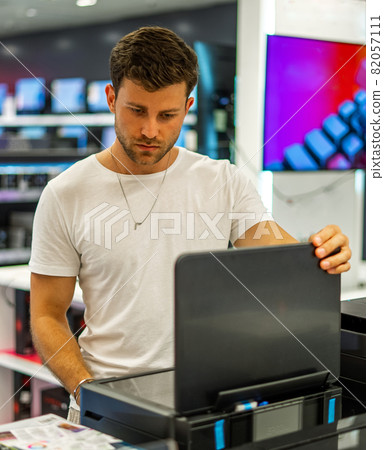 Young bearded male client in casual clothes checking quality of printer while choosing device in spacious electronics shop 82057111