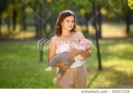 Breastfeeding in public park by young mother outdoors. 82057230