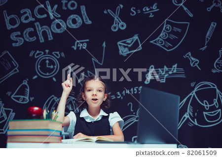 Emotional schoolgirl raises hand up with pen. Sitting with laptop . Distance education Emotional schoolgirl raises hand up with pen. Sitting with laptop . Distance education 82061509