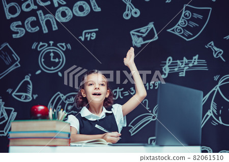 Caucasian schoolgirl raises hand up sits at laptop during online lesson. Distant School Learning. Caucasian schoolgirl raises hand up sits at laptop during online lesson. Distant School Learning. 82061510