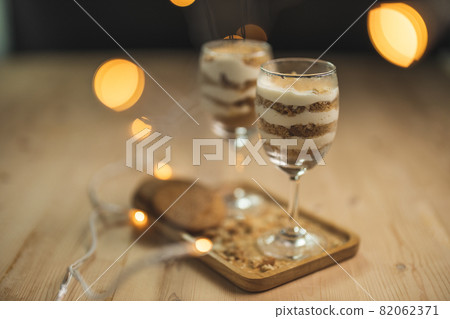 A wine glass fill with cream and crumb serve on a wooden plate with blurry background. A wine glass fill with cream and crumb serve on a wooden plate with blurry background. 82062371