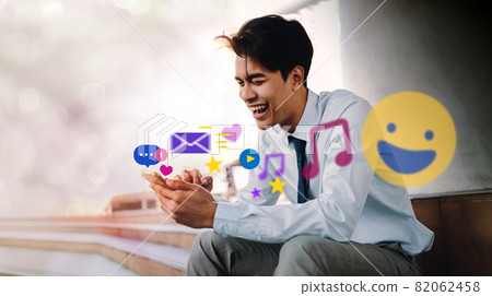 Smiling Young Asian Businessman Using Mobile Phone in the City. Enjoying Social Media application. surrounded by many icons Smiling Young Asian Businessman Using Mobile Phone in the City. Enjoying Social Media application. surrounded by many icons 82062458