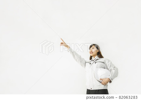 Standing in front of a white background, pointing diagonally upwards, staring at a young woman in work clothes 82063283