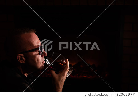 Mature man drinking cognac by the fireplace. 82065977