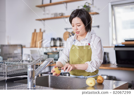 A young woman in an apron peeling potatoes in the kitchen 82067299