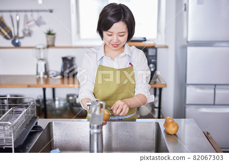 A young woman in an apron peeling potatoes in the kitchen 82067303