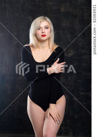 Young blonde plump woman with bright makeup in black bodysuit at dark background 82068931