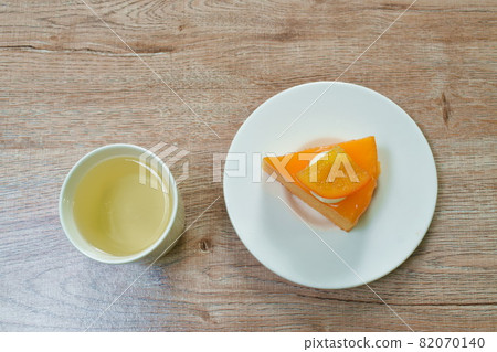 orange cake with cream topping fruit and hot tea cup on table 82070140