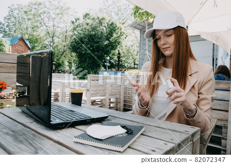 Redhead business woman using antiseptic gel to disinfect hands over a work desk in an outdoor workplace. Preventive measures during the period of pandemic and social exclusion. Redhead business woman using antiseptic gel to disinfect hands over a work desk in an outdoor workplace. Preventive measures during the period of pandemic and social exclusion. 82072347
