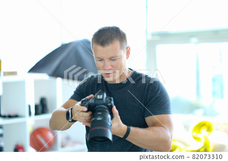 Male photographer holding black professional camera in his hands in studio Male photographer holding black professional camera in his hands in studio 82073310