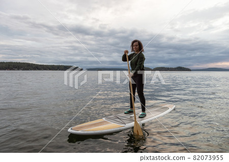 Adventurous White Caucasian Adult Woman Paddle Boarding in the Pacific Ocean 82073955