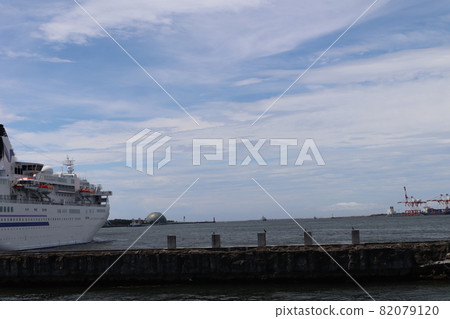 A landscape of a harbor where passenger ships stop, a jetty, a dome, a lighthouse, a crane, a ship, and a blue sky with many thin clouds in the distance. 82079120