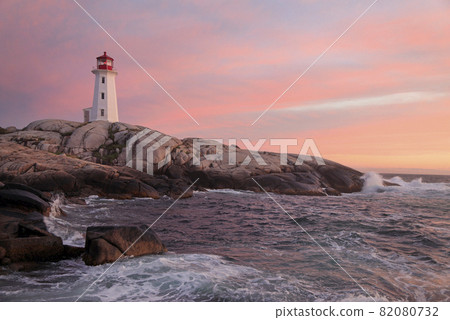 Peggy Cove Lighthouse illuminated at sunset with dramatic waves on the foreground, Nova Scotia, Canada 82080732