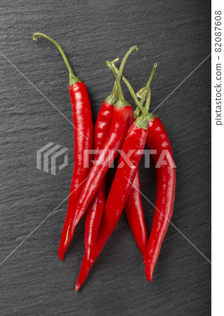 Pods of red chili peppers on a dark background Pods of red chili peppers on a dark background 82087608