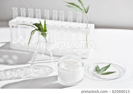 cannabis face cream and hemp leaves in laboratory . petri dishes and glassware on lab table. dermatology concept, alternative treatment. front view. 82088013