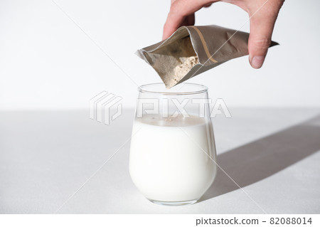 hand holding collagen powder travel pack and adding it to a milk to make protein cocktail. collagen peptides powder for healthy milkshake. joints care. 82088014