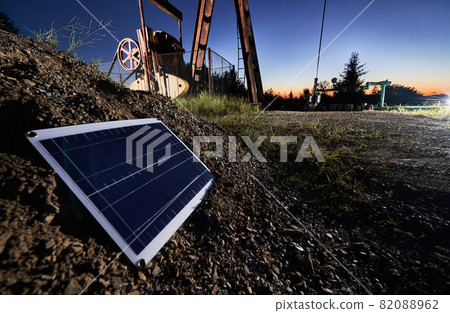 Close up view of one small solar panel, which located on stone mound. The lower part of oil well on the background. Concept of solar energy as alternative to oil production. Close up view of one small solar panel, which located on stone mound. The lower part of oil well on the background. Concept of solar energy as alternative to oil production. 82088962