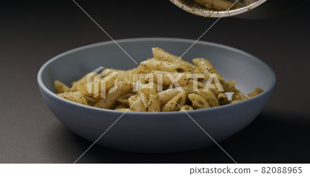pesto penne fall into blue bowl on black background 82088965