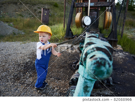 Adorable child in construction helmet using industrial wrench while repairing pipe of oil well pump jack. Cute kid oil worker tightening bolt on pipe. Concept of petroleum industry and childhood. Adorable child in construction helmet using industrial wrench while repairing pipe of oil well pump jack. Cute kid oil worker tightening bolt on pipe. Concept of petroleum industry and childhood. 82088966