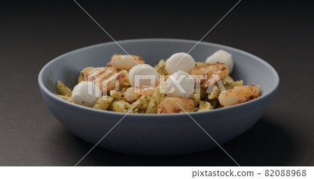 add mozzarella balls to pesto penne with shrimps in blue bowl on black background add mozzarella balls to pesto penne with shrimps in blue bowl on black background 82088968