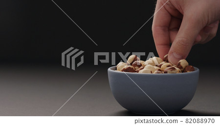 man hand take roasted hazelnuts from blue bowl on black background man hand take roasted hazelnuts from blue bowl on black background 82088970