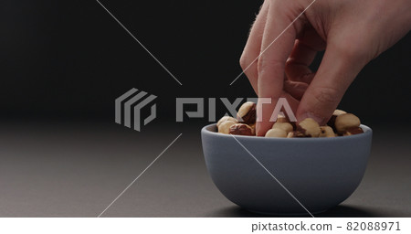 man hand take roasted hazelnuts from blue bowl on black background man hand take roasted hazelnuts from blue bowl on black background 82088971